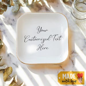 May include: White ceramic trinket tray with a gold rim. The tray has the text "Your Customized Text Here" written in black cursive.