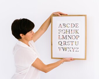 Può includere: Una stampa incorniciata dell'alfabeto con disegni floreali. Ogni lettera è composta da fiori rosa e bianchi e foglie verdi.