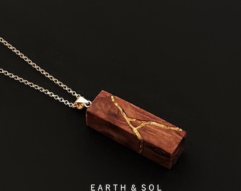 May include: A gold chain necklace with a rectangular pendant. The pendant is made of dark brown wood with gold-colored accents. The text "EARTH & SOL handmade in England" is visible.