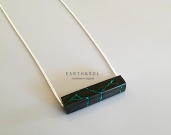 Puede incluir: Collar de cadena plateada con un colgante rectangular negro con incrustaciones turquesas en forma de grietas. El texto "EARTH & SOL Handmade in England" es visible en el fondo.