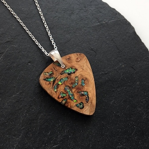 Puede incluir: Un collar de cadena de plata con un colgante de madera con forma de púa de guitarra. El colgante está incrustado con ópalo verde y azul iridiscente.