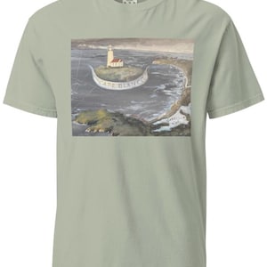 May include: Sage green t-shirt featuring a coastal scene with a lighthouse on a small island. The image includes the text "CAPE BLANCO" on a banner. The artwork depicts a lighthouse, ocean, and coastline.