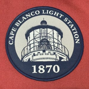 May include: A blue and white embroidered patch with a lighthouse and the text "Cape Blanco Light Station 1870".