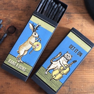 May include: Two matchboxes with illustrations of animals playing musical instruments. The first box features a rabbit with antlers playing a cymbal and the text "Band-a-Gong". The second box features a cat playing a cello and the text "Get it on".
