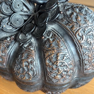 May include: A dark brown, intricately carved decorative box with a pumpkin shape. The box features detailed floral and scrollwork patterns, with a dark, almost black, finish. The lid has a decorative, circular design.
