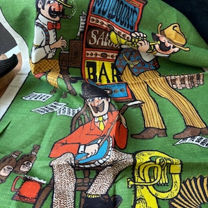 May include: Green fabric featuring a cartoon saloon scene with musicians and instruments. The text "Muldons Saloon Bar" is visible. The characters are dressed in colourful outfits.