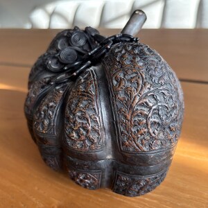 May include: A dark brown, intricately carved wooden container shaped like a pumpkin. The surface is covered in detailed floral and vine patterns. The container has a stem and a decorative top, suggesting it may be a box or a decorative piece.