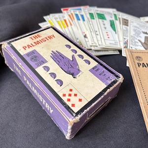 May include: A vintage "The Palmistry" card deck box in purple with a hand illustration. The box features the text "MOON SEVEN" and "MOON HAND INDOLENT TYPE". Several cards are visible in the background.