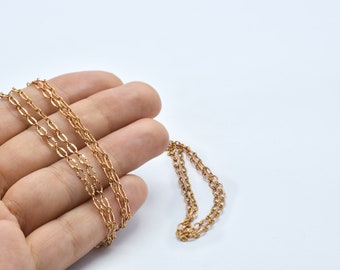 May include: A delicate gold-colored chain necklace with an intricate oval link design. The necklace is displayed on a white background, showcasing its fine details and warm hue. The chain is likely made of gold or a gold-toned metal.