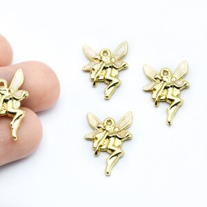 May include: Gold-colored fairy charms with white accents on the wings. The charms are in a sitting pose with a loop at the top for stringing. The image shows several charms on a white background.