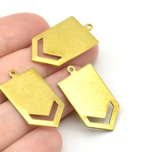 May include: Three brass-colored metal pendants with a geometric design. Each pendant is rectangular with a cut-out chevron shape and a small loop at the top for attaching to a chain or other jewelry component.
