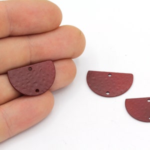 May include: Three burgundy-colored, semi-circular metal jewelry components with a textured surface and two holes each. One is held in a hand, while the others are on a white background. These components are suitable for jewelry making.