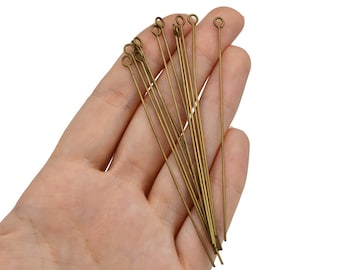 May include: A collection of antique brass eye pins, each with a looped end, held in a hand against a white background. These pins are ideal for jewelry making and crafting projects.