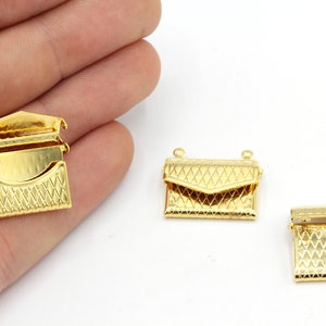 Op de afbeelding: Drie goudkleurige portemonneesluitingen. De sluitingen hebben een gestructureerd, geometrisch patroon. Eén sluiting is open en onthult de binnenkant. De andere twee sluitingen zijn gesloten. De sluitingen zijn klein, waarschijnlijk voor sieraden of kleine tassen.