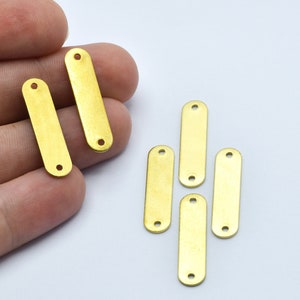 May include: Several small, rectangular brass metal tags with rounded ends and two holes. The tags are a bright gold color and appear to be new. The tags are shown on a white background.