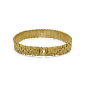 May include: A gold-colored bracelet with a woven design. The bracelet is circular and has a clasp closure. The woven pattern gives the bracelet a textured appearance. The jewelry is set against a white background.