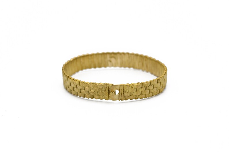 May include: A gold-colored bracelet with a woven design. The bracelet is circular and has a clasp closure. The woven pattern gives the bracelet a textured appearance. The jewelry is set against a white background.