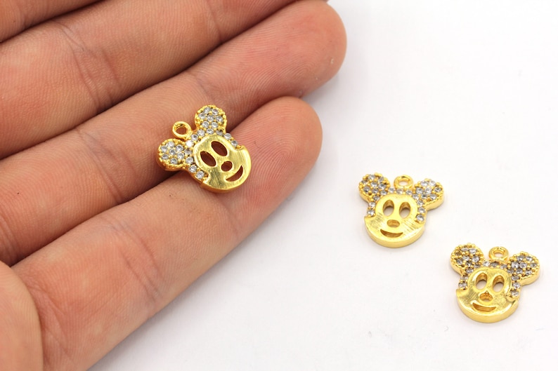 May include: Gold-colored Mickey Mouse charm pendants with clear crystal accents. The charms feature the iconic character's face and ears, with a loop for attaching to jewelry or other crafts. The charms are on a white background.