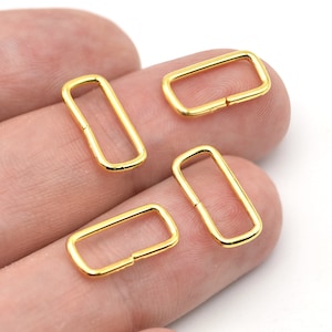 May include: Four gold-colored rectangular metal rings. Each ring has a rectangular shape with rounded corners and a small opening on one side. The rings are likely used for jewelry making or crafting.
