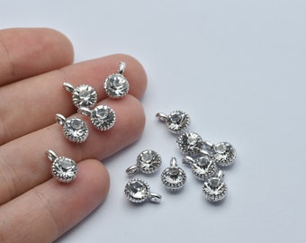 May include: A collection of small, silver-toned charms with clear, round crystals. Each charm has a loop at the top for attaching to jewelry. The crystals are faceted, catching the light and adding sparkle. These charms are ideal for DIY jewelry projects.