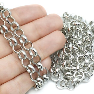 Könnte beinhalten: Nahaufnahme einer silberfarbenen Kette mit großen, abgerundeten Gliedern. Die Kette wird in einer Hand vor weißem Hintergrund gehalten. Die Kette hat eine helle, glänzende Silberfarbe.