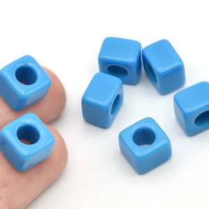 Puede incluir: Seis cuentas cuadradas de color azul claro con un agujero en el centro. Las cuentas están hechas de un material brillante y están dispuestas sobre un fondo blanco. Estas cuentas son ideales para la fabricación de joyas y manualidades.