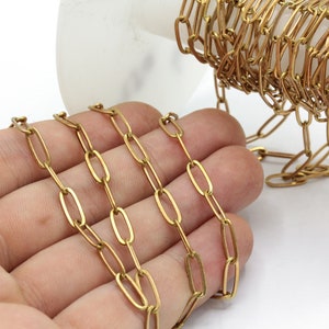 Könnte beinhalten: Nahaufnahme einer goldfarbenen Kette mit ovalen Gliedern. Die Kette wird in einer Hand gezeigt, wobei ein Teil der Kette im Hintergrund aufgerollt ist. Die Kette ist aus Metall.