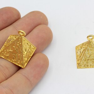 May include: Two gold-colored pyramid pendants with intricate hieroglyphic designs. The pendants have a loop at the top for hanging. The pyramids are displayed on a white background.
