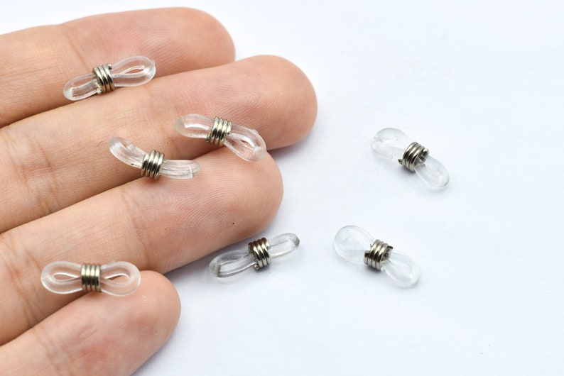 Puede incluir: Retenedores de gafas transparentes, de forma ovalada, con espirales de metal plateado. Estos peque&ntilde;os accesorios transparentes est&aacute;n dise&ntilde;ados para asegurar las gafas. Varios retenedores est&aacute;n sobre una superficie blanca.
