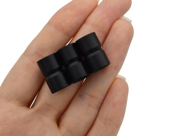 May include: A cluster of six small, black, cylindrical objects with a flared top are held in an open hand. The objects are made of a smooth, matte material. The background is white. The items are likely components or accessories.