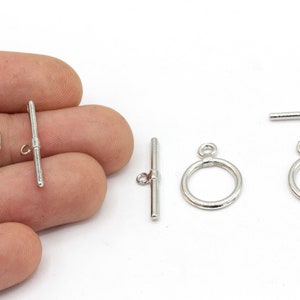 May include: Silver-colored toggle clasps, a jewelry component, are displayed against a white background. The clasps include a circular ring with a loop and a straight bar with a small loop. The clasps are shown in various orientations.