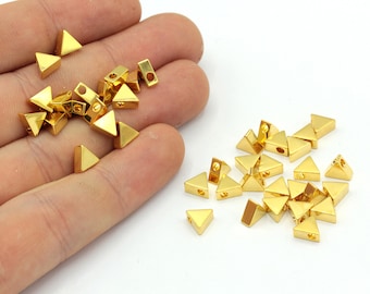 May include: Gold-colored metal triangle beads with a hole at the top for stringing. The beads are small, with a triangular pyramid shape. The beads are shown on a white background.