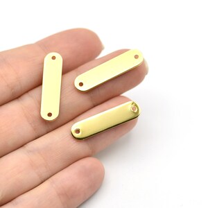 May include: Close-up of three gold-colored rectangular metal jewelry tags. Each tag has rounded ends and two small holes for attaching to other jewelry components. The tags are displayed against a white background.