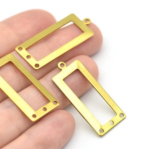 Könnte beinhalten: Drei rechteckige Schmuckzubehörteile aus Messing mit einem ausgeschnittenen Mittelteil und kleinen Löchern zur Befestigung. Jedes Zubehörteil hat oben eine kleine Schlaufe. Die Zubehörteile sind goldfarben.