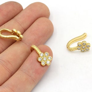 May include: Gold-colored jewelry findings with a floral design. The findings have a flower-shaped charm with clear, round gemstones. The findings are small and delicate, with a curved hook.
