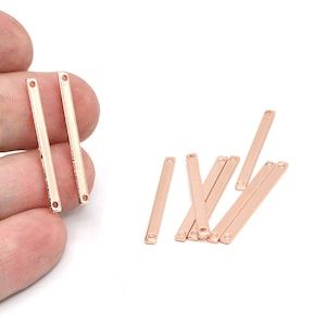 May include: Rose gold-colored metal bar charms with small holes at each end. Some charms have a line of small, clear stones. These jewelry-making components are shown against a white background.