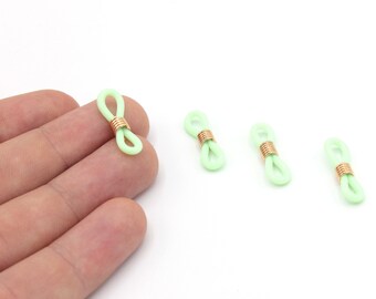 May include: Four light green eyeglass retainers with gold-colored metal coils. One retainer is held by a hand. The retainers are made of a soft, flexible material and are designed to keep glasses secure.