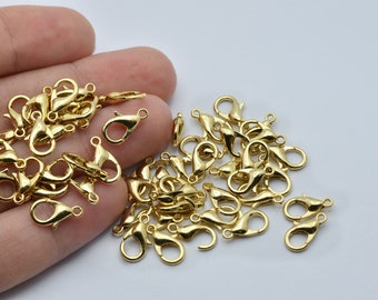 Puede incluir: Una colección de pequeños cierres de langosta dorados y brillantes. Estos cierres se utilizan para la fabricación de joyas y están diseñados para sujetar de forma segura collares, pulseras y otros accesorios. Los cierres se muestran sobre un fondo blanco.