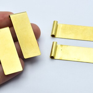 Può includere: Quattro etichette rettangolari in metallo color oro con un anello piegato a un'estremità. Le etichette sono di un colore oro brillante e sembrano nuove. Le etichette sono probabilmente per la creazione di gioielli o l'artigianato.