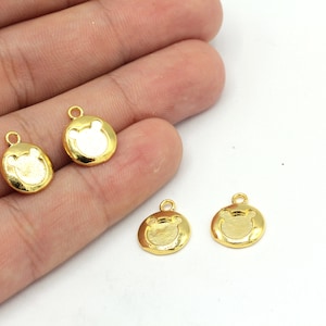 May include: Four small, gold-colored bear-shaped charms. Each charm has a circular shape with a bear face design in the center and a small loop at the top for attaching to jewelry or other crafts. The charms are on a white background.