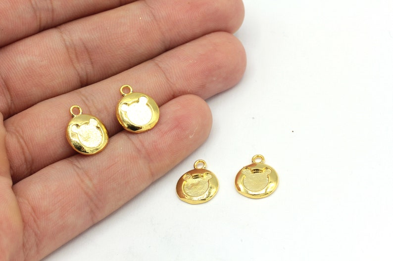 May include: Four small, gold-colored bear-shaped charms. Each charm has a circular shape with a bear face design in the center and a small loop at the top for attaching to jewelry or other crafts. The charms are on a white background.