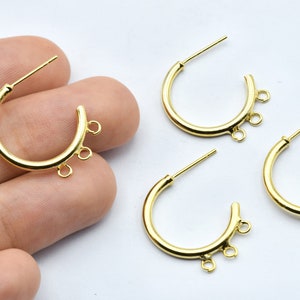 May include: Gold-colored hoop earrings with three small loops at the bottom of the hoop. The earrings have a post for insertion into the ear. The earrings are on a white background.