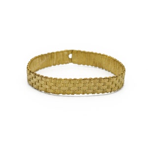 May include: A gold-colored bracelet with a woven design. The bracelet is approximately 7 inches in circumference and has a rectangular pattern. The clasp is a small hole. The bracelet is set against a white background.