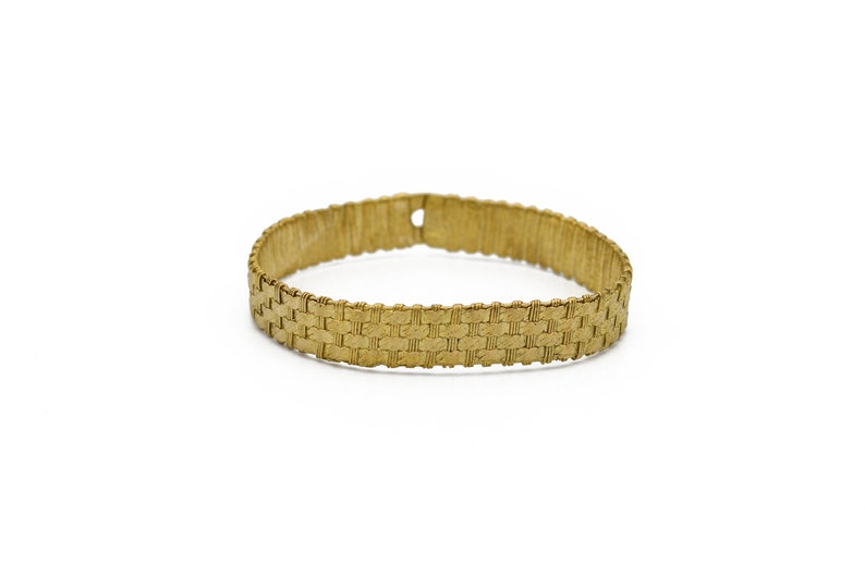 May include: A gold-colored bracelet with a woven design. The bracelet is approximately 7 inches in circumference and has a rectangular pattern. The clasp is a small hole. The bracelet is set against a white background.