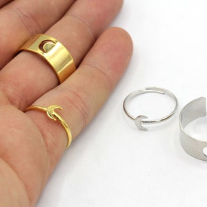 May include: A collection of rings featuring a crescent moon design. The rings are in gold and silver tones, with varying styles including a wide band, a delicate band, and an adjustable open ring.