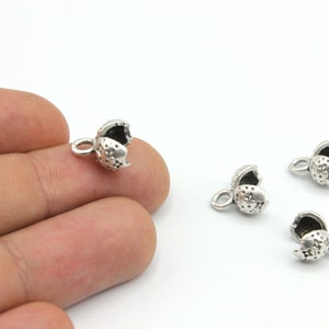 May include: Close-up of several small, silver-coloured jewellery findings. Each finding is shaped like a small, open clam shell with a loop for attaching to other jewellery components. The findings have a textured surface and are on a white background.