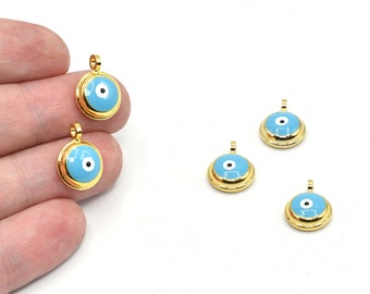Puede incluir: Colgantes redondos dorados con un diseño de ojo azul claro. Los colgantes tienen un borde dorado y un pequeño lazo en la parte superior para sujetarlos a una cadena u otras joyas. El ojo tiene un iris blanco y una pupila negra.