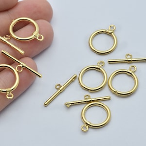 May include: Several gold-colored toggle clasps, each consisting of a circular ring and a straight bar with a perpendicular bar. The clasps are designed for jewelry making and crafting. The clasps are shown against a light background.