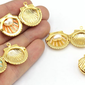 May include: Gold-colored seashell-shaped pendants with hinged openings. Each pendant features a pearl-like bead inside, with interior colors of orange and blue. The pendants are designed for jewelry making or crafting.