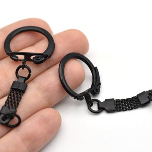 May include: Two black metal keychains with a mesh design. Each keychain has a circular ring and a rectangular mesh section with a small ring at the end. The keychains are shown against a white background.